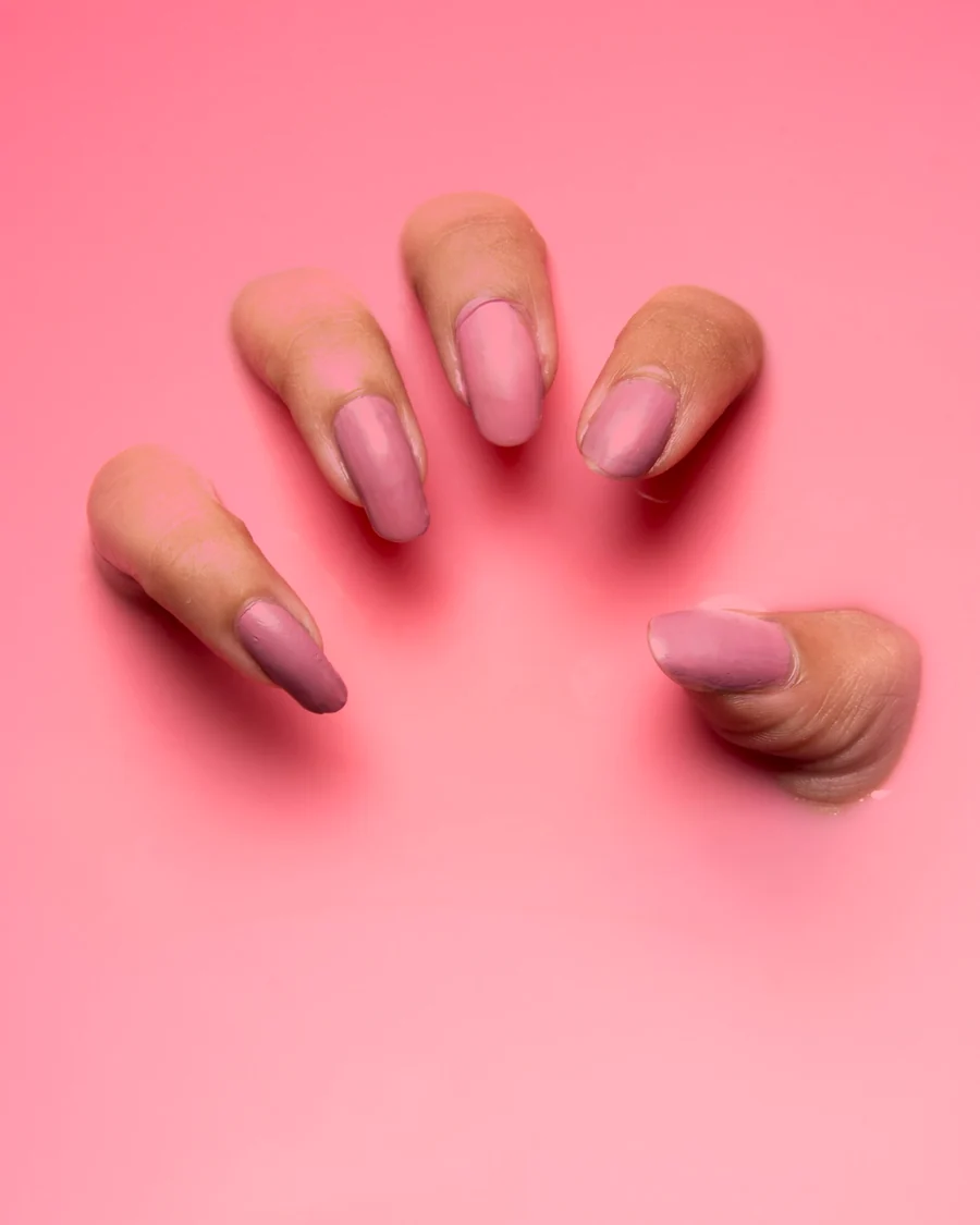 Mão com unhas esmaltadas em rosa suave sobre um fundo rosa