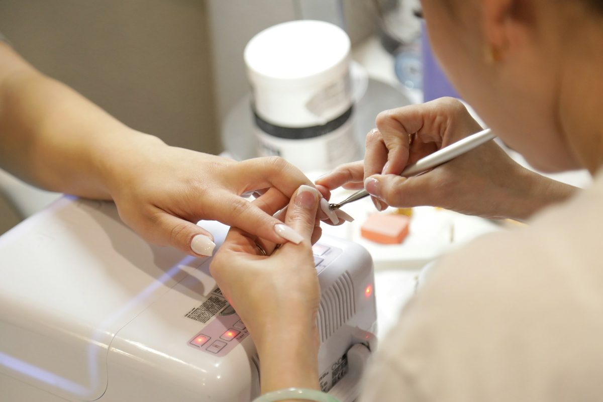 Nail designer finalizando unhas em gel na cabine UV durante o atendimento